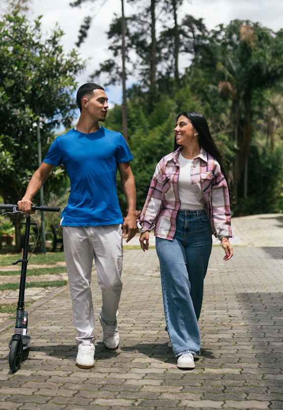 A man and a woman are walking together, the man is holding a scooter.
