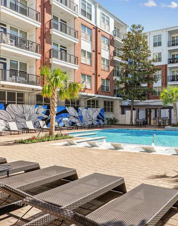 A pool surrounded by lounge chairs and palm trees.