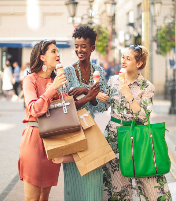 Three women are standing on a street, one of them is holding a bag.