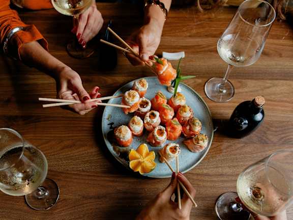 A group of people are gathered around a plate of sushi.