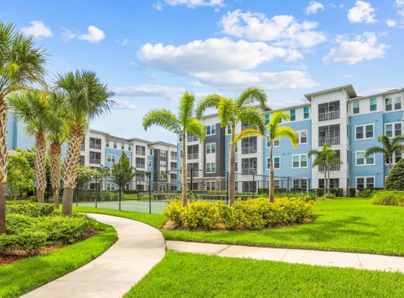 Sidewalk surrounded by luscious green landscape and palm trees at Dunedin Commons apartments in Dunedin, FL