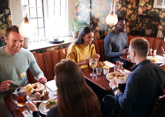 A group of people are sitting around a table eating food and drinking beer.