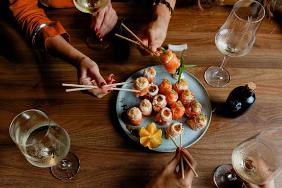 A group of people are gathered around a plate of sushi.