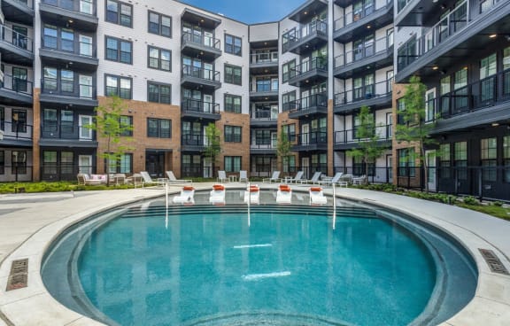 an outdoor pool with lounge chairs and an apartment building in the background
