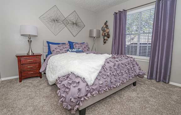 A bedroom with a bed, nightstand, and window at The Oasis apartments in Bossier City, LA