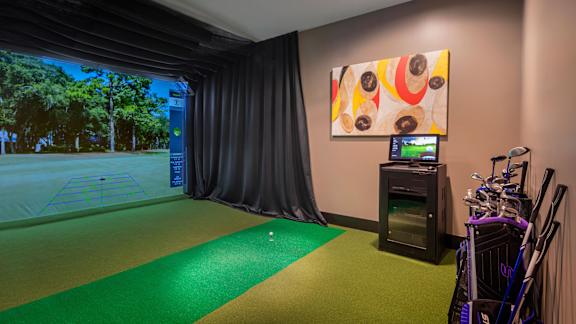 A room with a golf simulator and a painting on the wall.