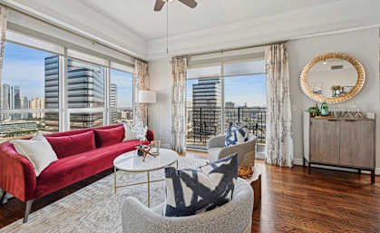 Model living room with a red couch, a white coffee table, and a large window with a view of the city at Dominion Post Oak apartments in Houston, TX