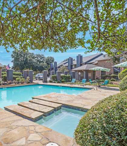 A swimming pool surrounded by a stone patio and green bushes.