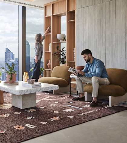 A man is sitting on a chair in a living room with a city view through the window.