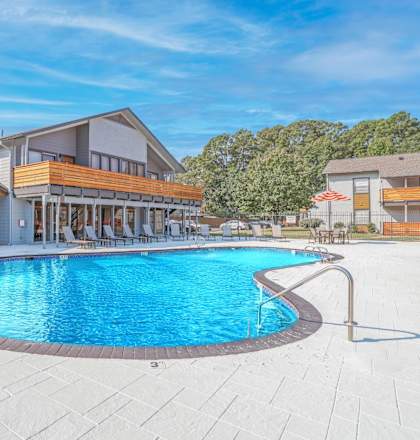 A large outdoor swimming pool surrounded by a patio area with lounge chairs and umbrellas at The Marq apartments in Shreveport, LA
