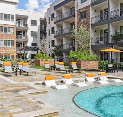 A pool surrounded by orange chairs and buildings in the background.