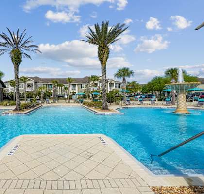 A large swimming pool surrounded by palm trees and residential buildings.