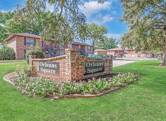 A brick sign that reads "Orleans Square" is surrounded by flowers and greenery at Orleans Square in Shreveport, LA