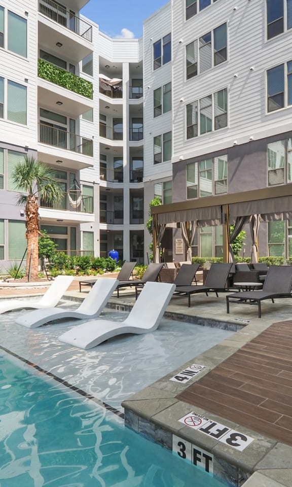 a pool with lounge chairs and a tree in front of an apartment building