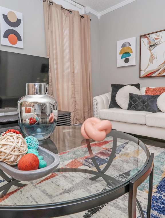 Model living room furnished with a couch, coffee table, TV, and paintings at Maplewood apartments in Shreveport, LA.