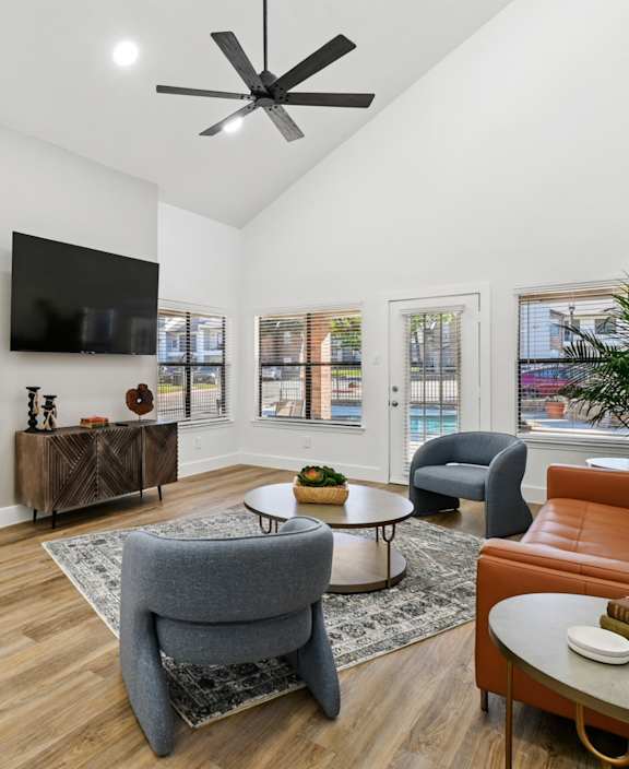 A living room with a grey armchair, a brown leather couch, a wooden coffee table, and a flat screen TV mounted on the wall.