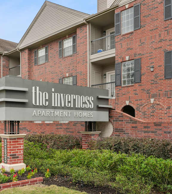 A sign for The Inverness Apartment Homes is displayed in front of a brick building.
