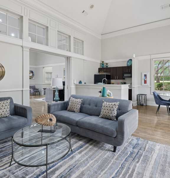 A living room with a grey couch, a glass coffee table, and a round mirror on the wall.