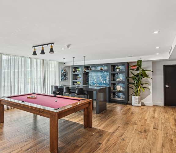 A pool table with a red cloth is in the middle of a room with a wooden floor.