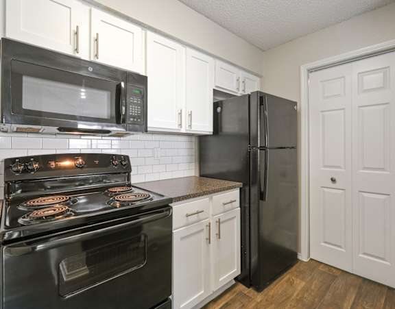 A black stove and microwave in a kitchen with white cabinets.