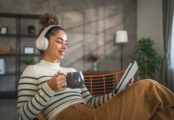 A woman in a striped sweater is sitting with a mug and a tablet.
