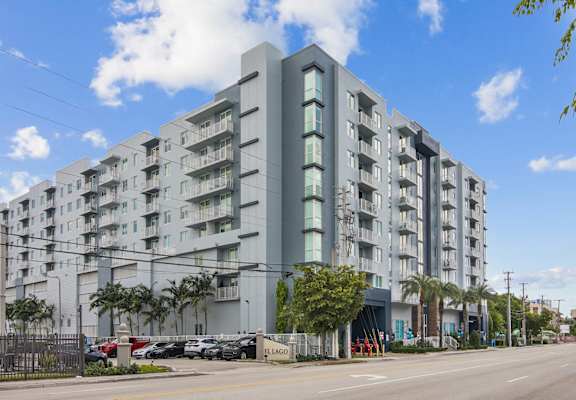 A large grey apartment building with a parking lot in front.