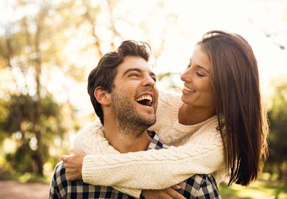 A man is giving a woman a piggyback ride in a park.