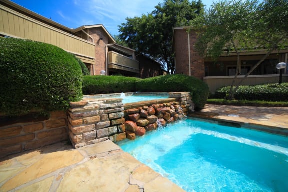 a swimming pool with a stone wall and a waterfall in front of a brick building