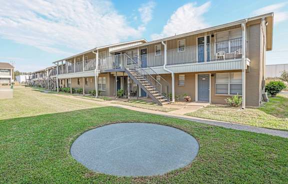 A round concrete structure is in the middle of a grassy area in front of apartment buildings.