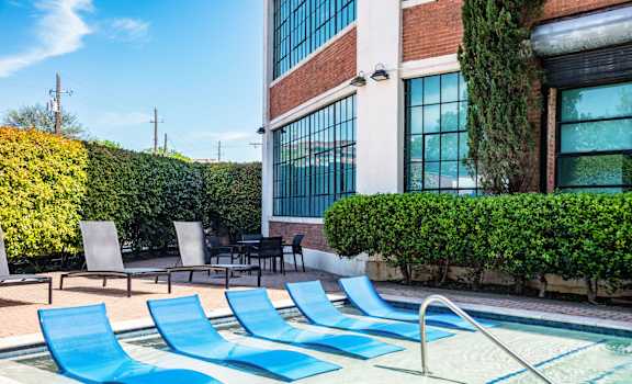 a pool with blue chaise lounge chairs in front of a brick building