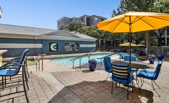 A pool area with chairs and a yellow umbrella at Encore at Buckingham Apartments in Richardson, TX
