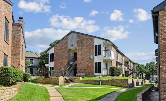 An apartment building with green lawns in front at The Oaks of Denton Apartments in Denton, TX