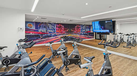 Cycling studio in gym with a row of stationary bikes and a TV at Twenty2 West luxury apartments in Miami, FL