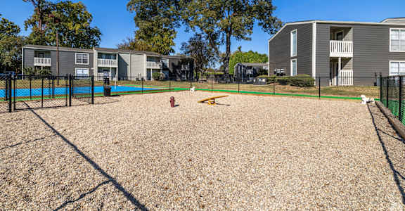A dog park with a sandy area and a fence in front of apartment buildings at Maplewood apartments in Shreveport, LA.