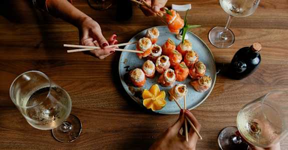 A group of people are gathered around a plate of sushi.
