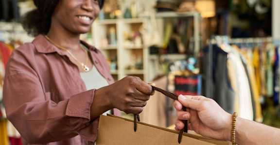 A woman in a pink shirt is handing over a brown paper bag to another person.