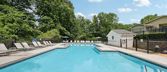 A large swimming pool surrounded by trees and lounge chairs at Gwinnett Square Apartments in Duluth, GA