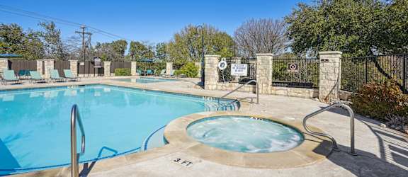 Our sparkling pool with a hot tub and poolside seating at On the Green apartments in Austin, TX