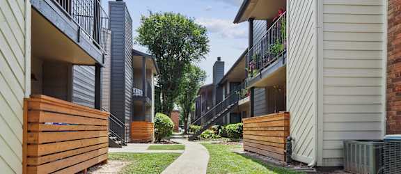 a path between two buildings with a wood fence on the left and a brick building on the