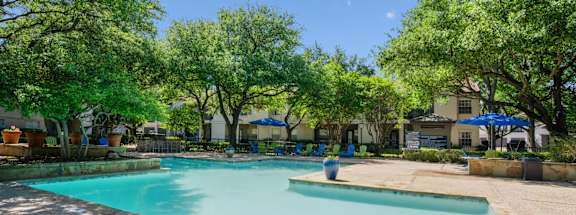 A pool surrounded by trees and poolside seating at La Costa in Plano, TX