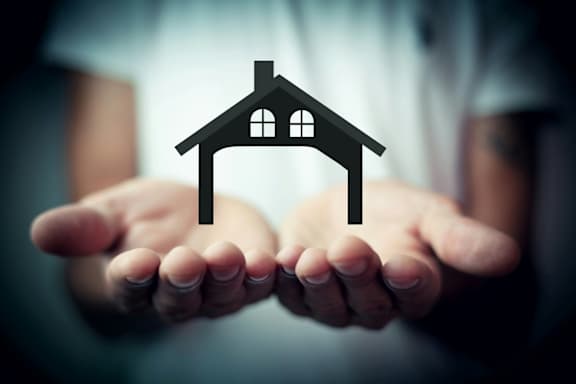 A person is holding a small house icon in their outstretched hands.
