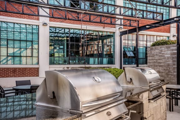 an outdoor patio with two bbq grills and a building in the background