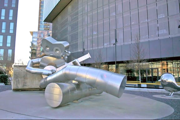 a large metal sculpture of a robot laying on top of a suitcase