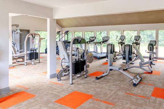 A gym with orange mats and a variety of exercise equipment.
