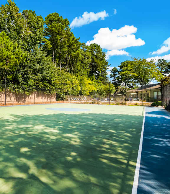 A tennis court surrounded by trees on a sunny day.