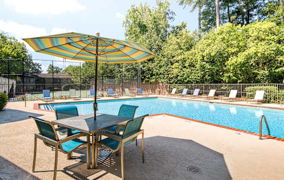 A table with chairs and an umbrella is in front of a pool.
