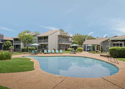 A swimming pool in a residential area surrounded by houses and lawn chairs.
