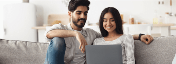 A man and woman are sitting on a couch looking at a laptop together.