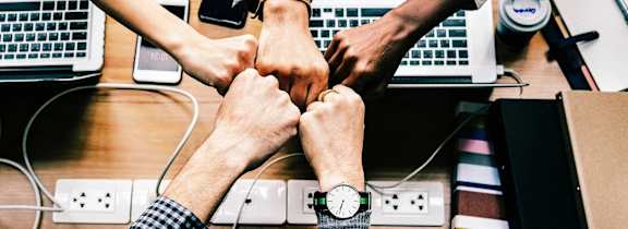 a group of people joining their hands over a desk with laptops