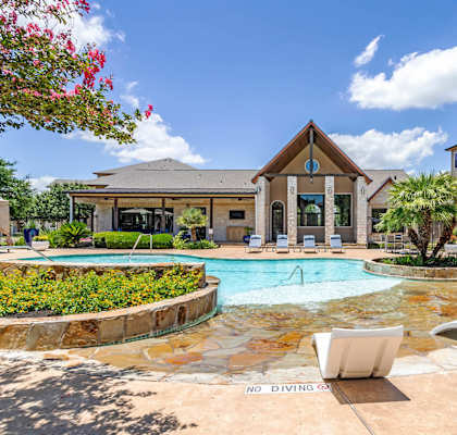 A pool surrounded by chairs and a building in the background.